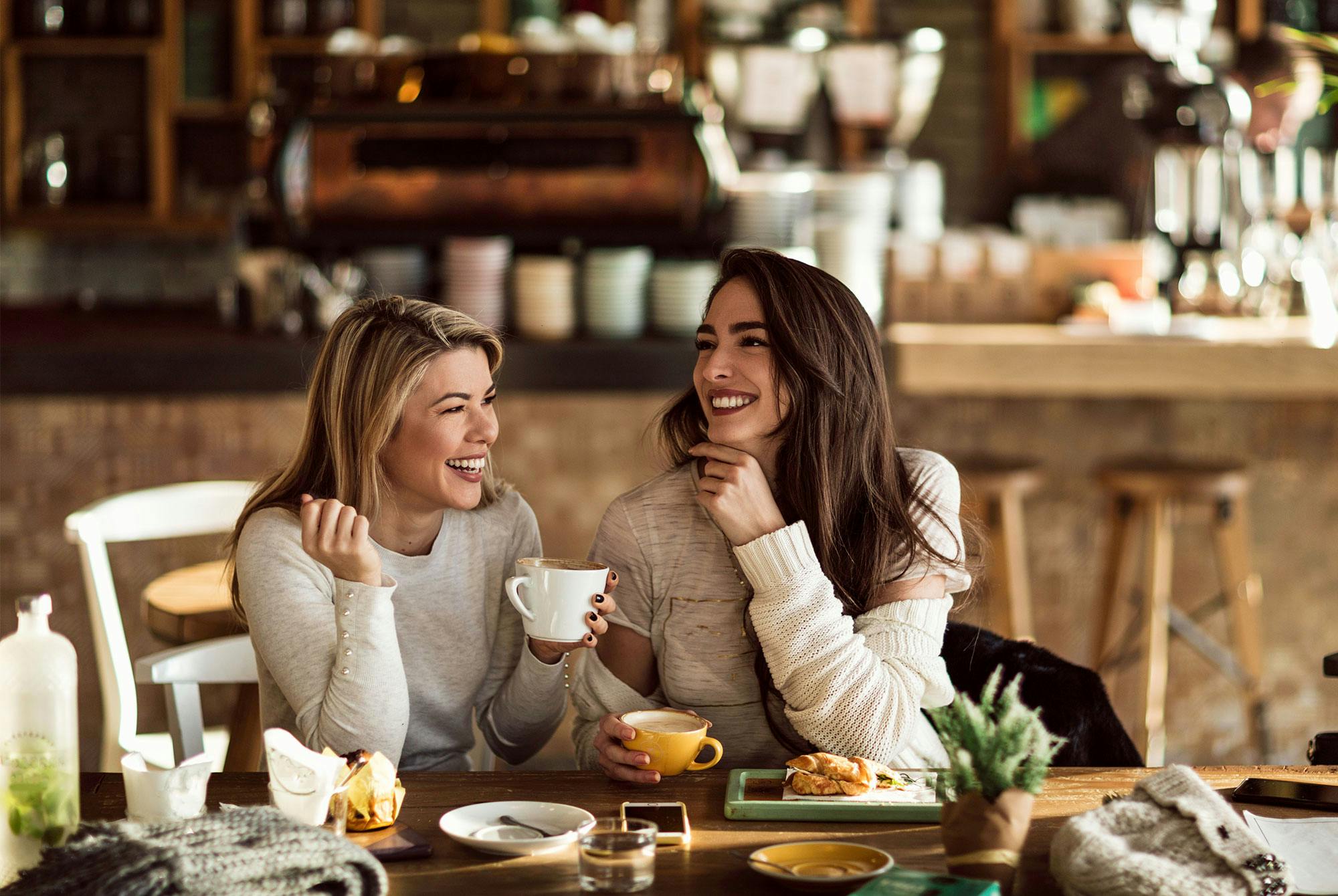 Två kvinnor skålar i kaffe. Både kaffe och sociala relationer är gynnsamt för hälsan.