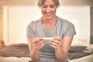 laskettu aika hedelmöityshoidoissa - iloinen nainen katselee positiivista raskaustestiä