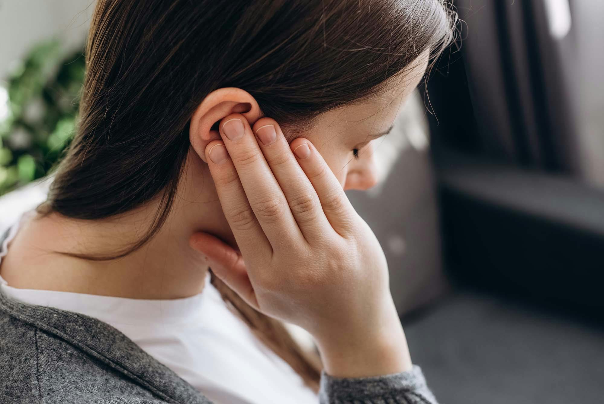 En kvinde holde sig for øret. Hun er frustreret, fordi hun har susen for ørene. Hun skal have råd om tinnitus.