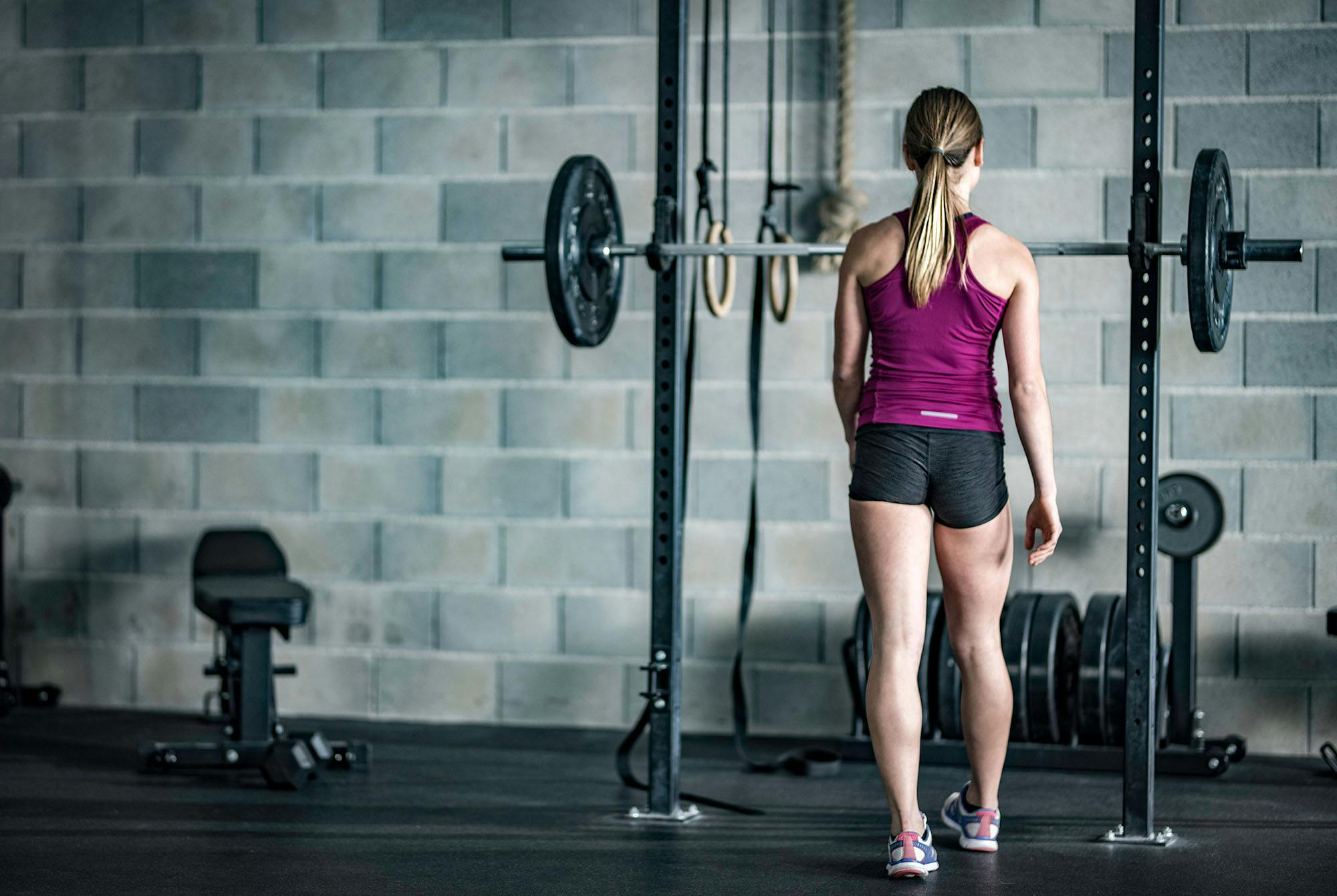 kvinde, der går hen imod et stativ med vægtstang.