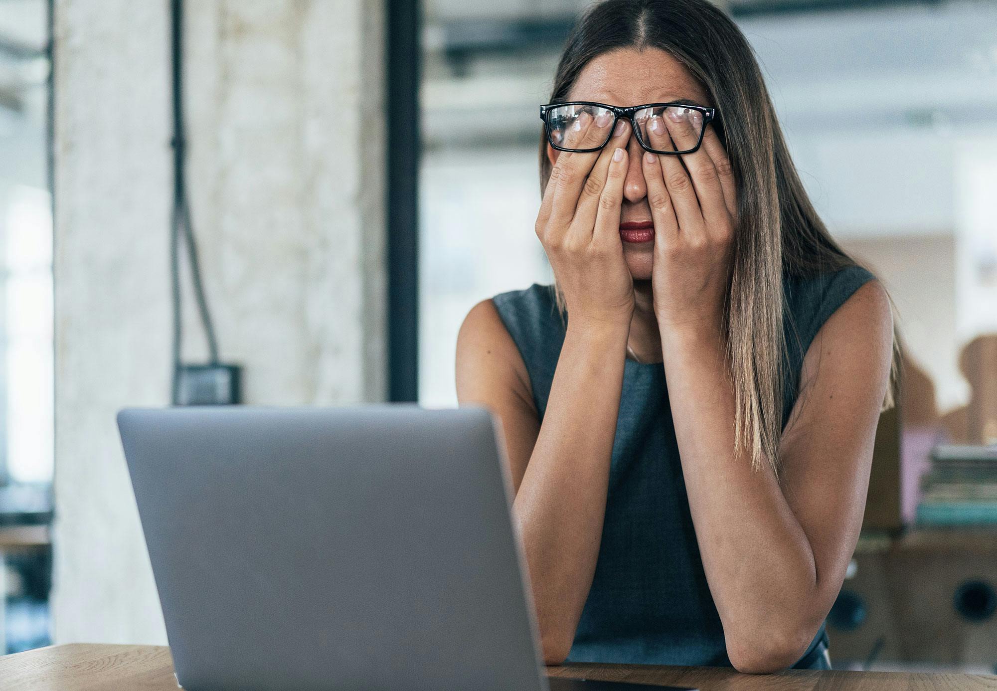 En kvinder holder hænderne op foran øjnene. Hun er stresset på arbejdspladsen.