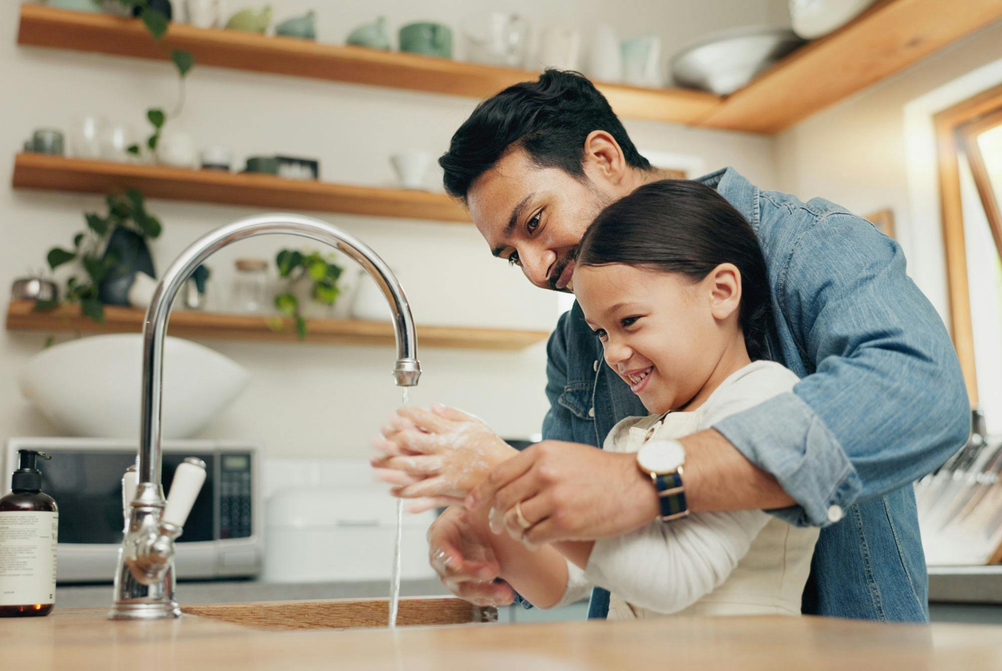 Jente vasker hendene på kjøkkenet sammen med faren – forebygger smitte