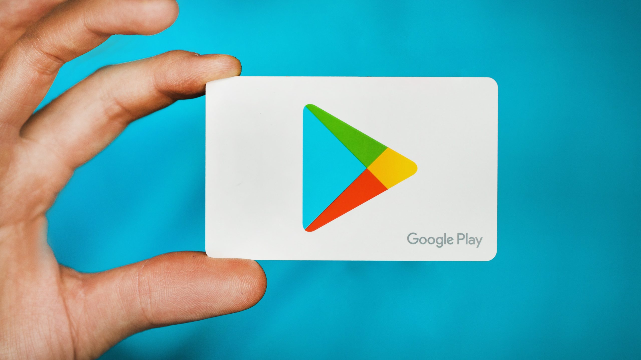 Hånd som holder et gavekort til Google Play Butikk mellom to fingre.