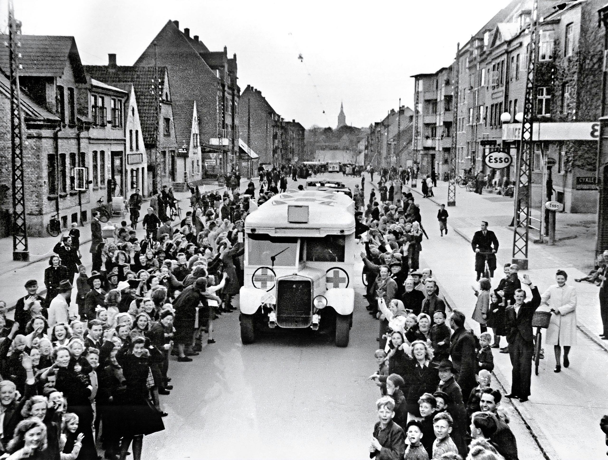 En av Folke Bernadotte-aktionens vita bussar plöjer igenom jublande folkskaror i Odense.